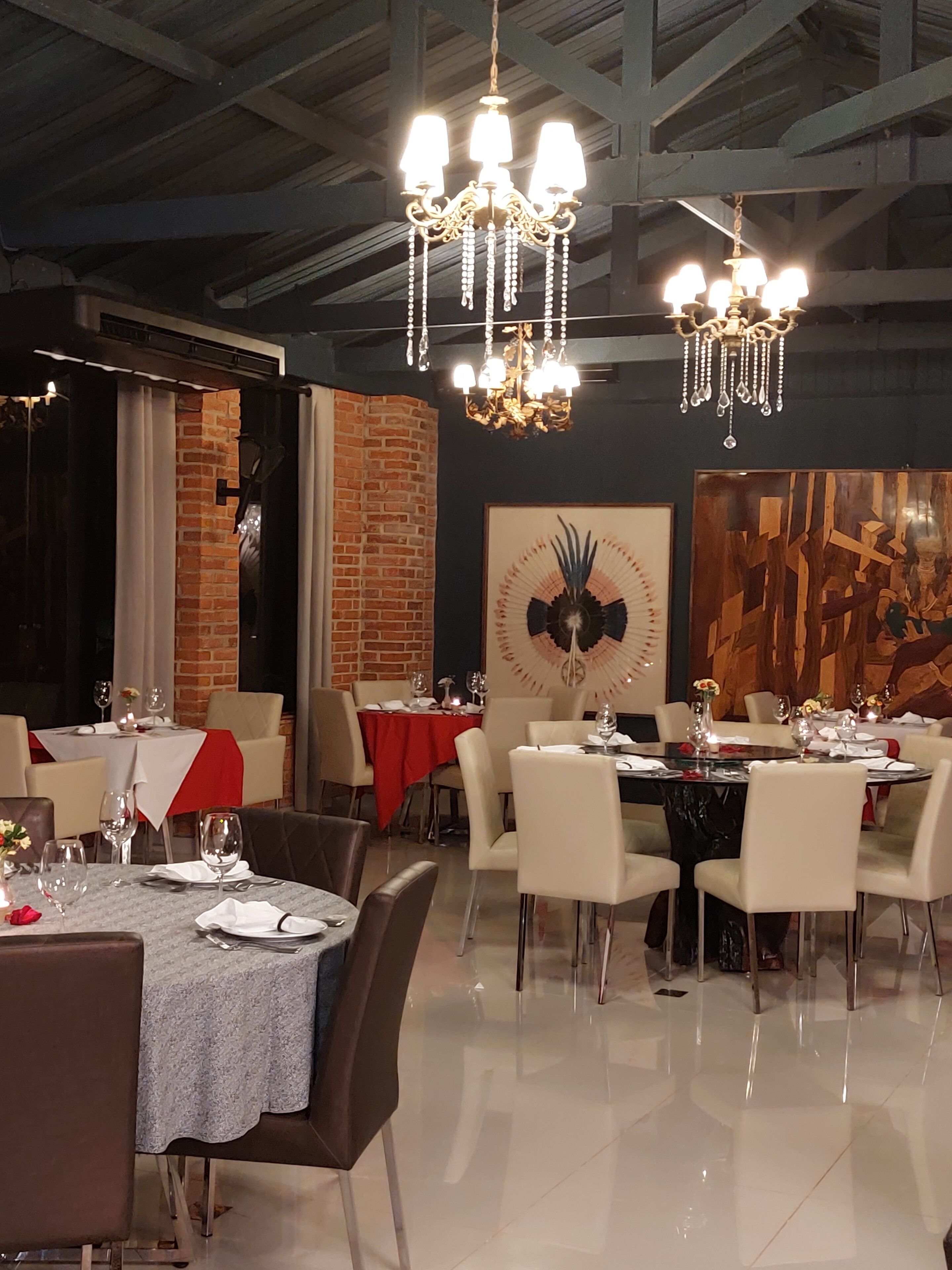 A dining area with tables set for four, a chandelier, and a brick wall.