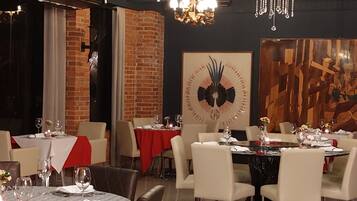 A dining area with tables set for four, a chandelier, and a brick wall.