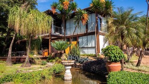 A two-story building with a balcony, surrounded by tropical vegetation and a small pond. - Pobore Pousada Spa Gastronomia (Rondonopolis)