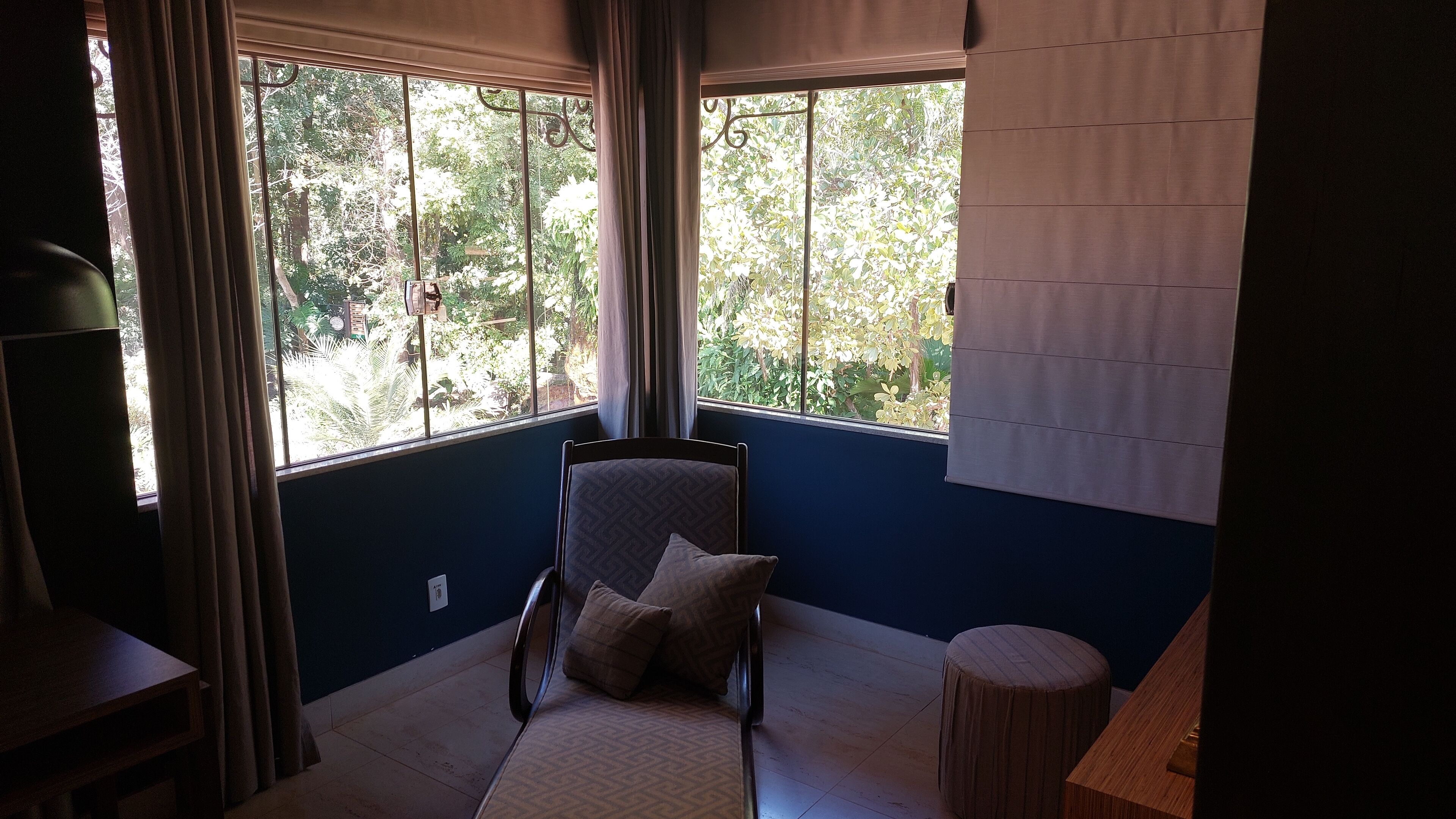Habitación accesible en silla de ruedas con vistas a árboles a través de amplias ventanas, una pequeña mesa redonda y una pared azul.