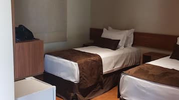 Quarto de hotel com duas camas, uma escrivaninha pequena e um ventilador de teto.