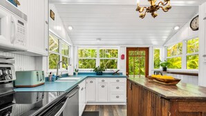 A kitchen with white cabinets, a black stove, a teal toaster, and a wooden island with a bowl of fruit. - The Seaside Treasure *Sparkling Pool w Guesthouse* (Stuart)
