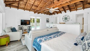 A spacious room with a high wooden ceiling, a large bed with a blue and white patterned bedspread, a white sofa, and a television on a white cabinet. - The Seaside Treasure *Sparkling Pool w Guesthouse* (Stuart)