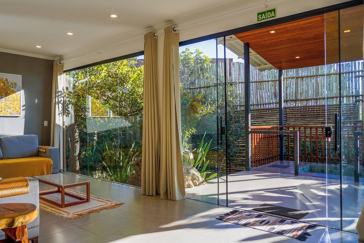 A modern hotel lobby with a sofa, a coffee table, and a glass partition with a view of greenery.