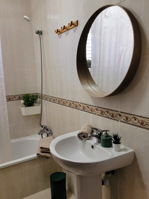 Ein Badezimmer mit weißem Waschbecken, einem runden Spiegel, einer Dusche und einer Toilette.