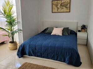 Ein ordentlich bezogenes Bett mit blauer Bettdecke, eine Weltkarte an der Wand und eine Topfpflanze neben dem Bett.