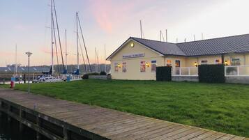 Un restaurant situé au bord de l’eau, avec un quai, des bateaux et une zone herbeuse.