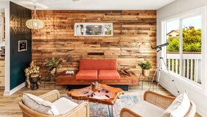 Una sala de estar acogedora con una pared de madera, un sofá rojo, sillas de mimbre y una mesa de centro.