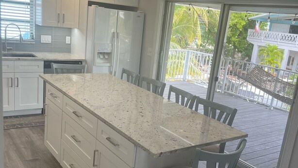 A modern kitchen with a large island, white cabinetry, and a view of the outdoor deck. - Special Rate Available August 2026 book now (Summerland Key)
