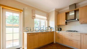 A kitchen with wooden cabinets, a tiled floor, and a window with blinds. - Villa Vita, Bright and Sunny Villa Located at Praia D'el Rey (Amoreira)
