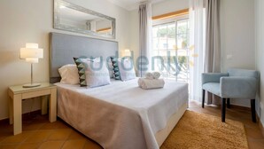 A hotel room with a large bed, a bedside table with a lamp, a chair, and a window with curtains. - Villa Vita, Bright and Sunny Villa Located at Praia D'el Rey (Amoreira)