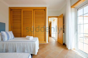 A hotel room with a bed, a small table, and a wardrobe. There is a window with curtains and a view of the outside. - Villa Vita, Bright and Sunny Villa Located at Praia D'el Rey (Amoreira)