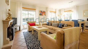 A living room with a sofa, coffee table, TV, and fireplace. There are windows with curtains and a painting on the wall. - Villa Vita, Bright and Sunny Villa Located at Praia D'el Rey (Amoreira)