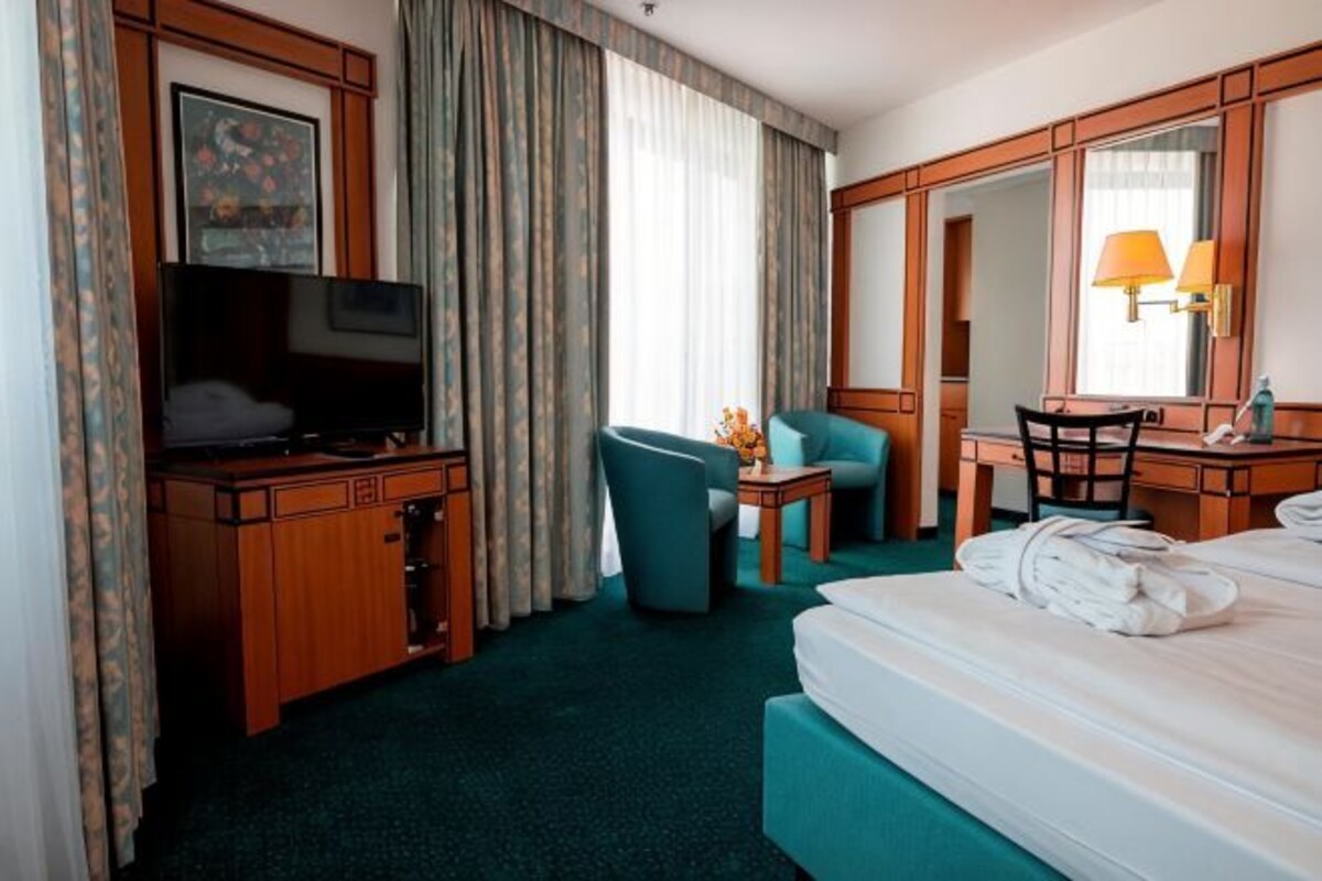 Una habitación de hotel con cama, escritorio, silla, televisor y un espejo grande.