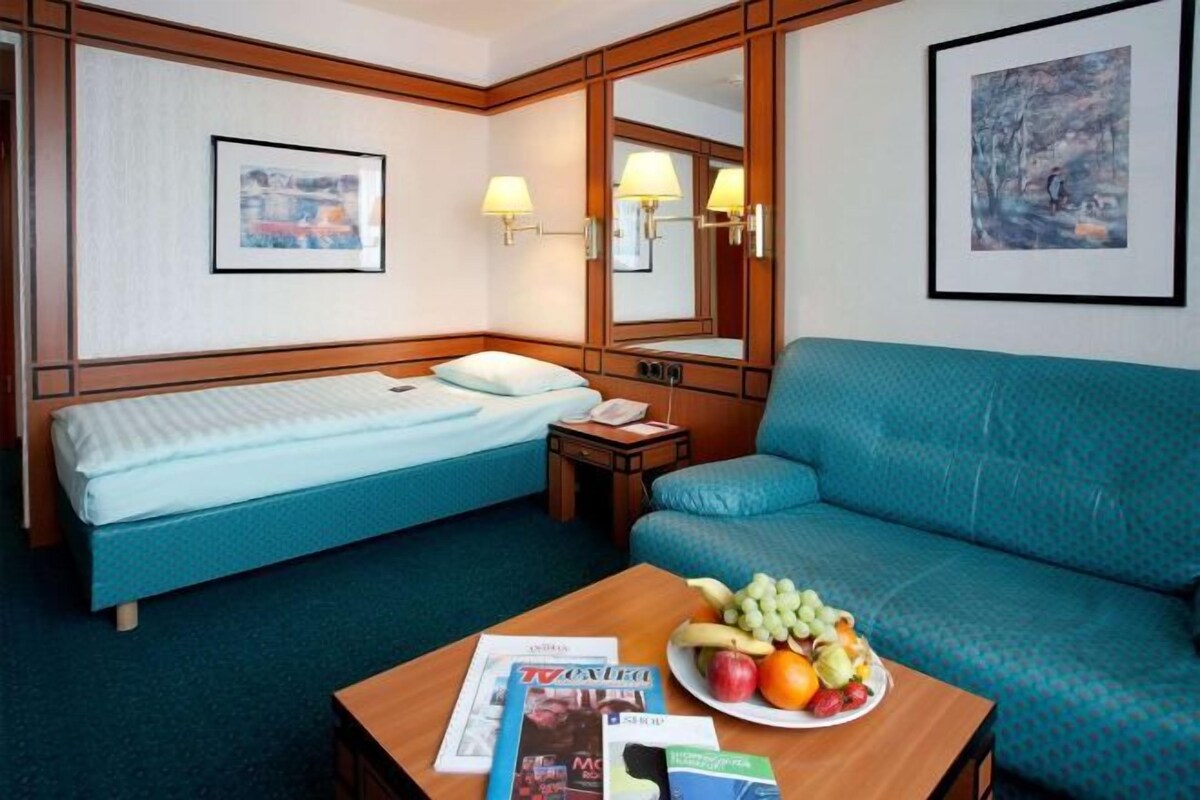 Una habitación de hotel con cama, sofá, una mesa con fruta y un espejo.
