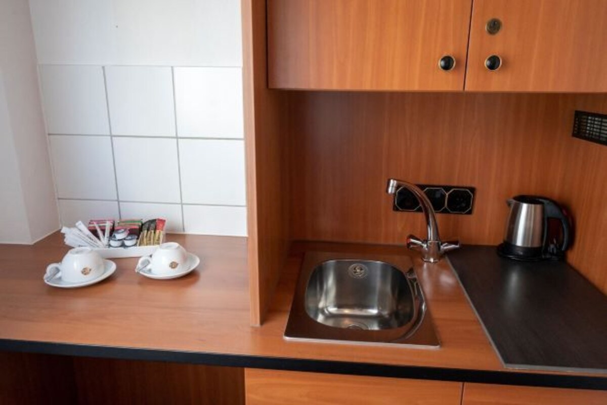 Una cocina con un lavamanos de acero inoxidable, una tetera y un juego de tazas sobre la encimera.