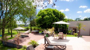 An outdoor patio area with lounge chairs, umbrellas, and a large tree providing shade. - 7 Saltos Resort (Salto del Guaira)