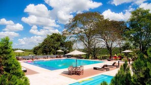 A large outdoor swimming pool with lounge chairs and umbrellas, surrounded by trees and greenery. - 7 Saltos Resort (Salto del Guaira)