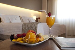 Una habitación de hotel con una cama bien hecha, un plato de fruta y un vaso de jugo de naranja sobre una mesa.