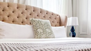 A neatly made bed with a tufted headboard, a patterned pillow, and a blue bedside lamp. - Rose Hill Inn (Versailles)