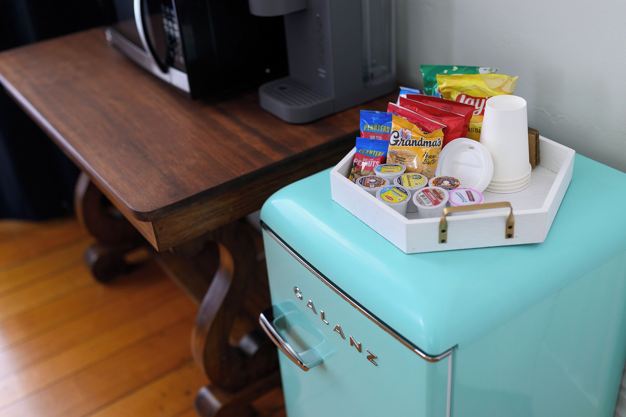 Un refrigerador verde azulado antiguo lleno de aperitivos y condimentos, una cafetera y un microondas sobre una mesa de madera.