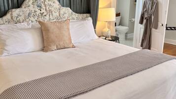 Cama bem arrumada com cabeceira estampada, abajur e roupão pendurado na porta.
