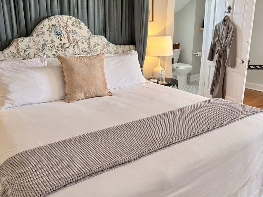 Cama bem arrumada com cabeceira estampada, abajur e roupão pendurado na porta.