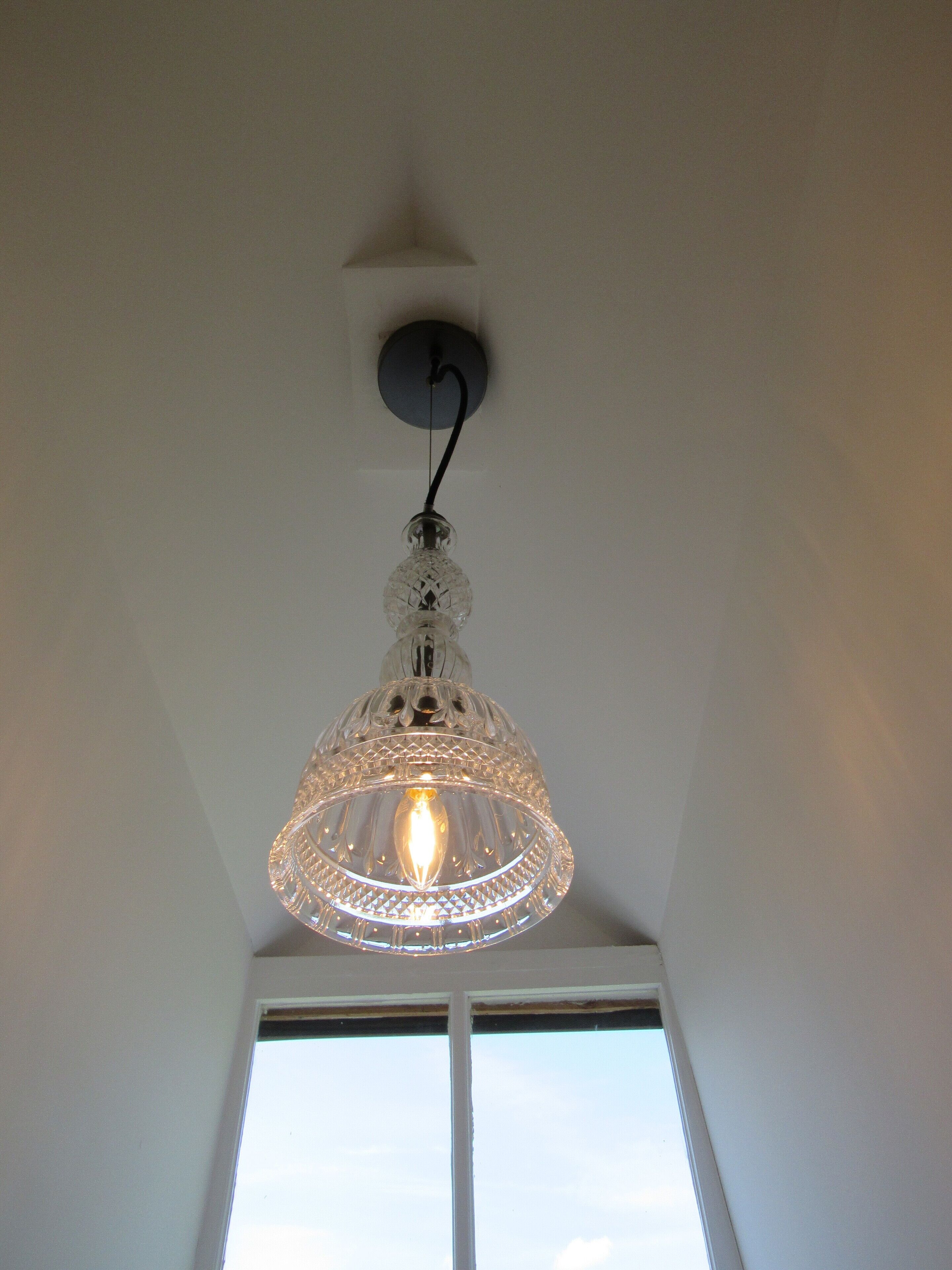 Un luminaire suspendu en verre transparent, fixé au plafond, avec une ampoule visible à l’intérieur.