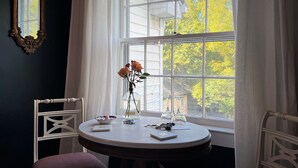 A room with a round table by a window, a vase with flowers, a bowl, and a book. - Rose Hill Inn (Versailles)