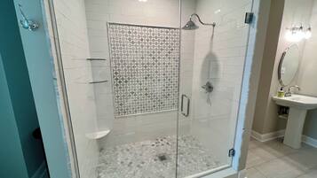 Un baño moderno con ducha de vidrio, paredes con azulejos blancos y mampara de ducha estampada.