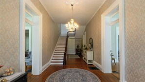 A grand hallway with a staircase, ornate chandelier, and patterned wallpaper. - Rose Hill Inn (Versailles)