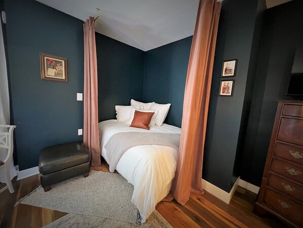 Une chambre à coucher avec un lit, une table de chevet, une commode et une fenêtre avec des rideaux.