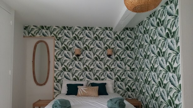 Ein Schlafzimmer mit einem Bett, einem Spiegel und einer Wand mit einem Blattmuster.