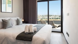 A modern hotel room with a large bed, a view of the city, and a balcony with chairs. - Aparthotel Adagio Malta Central (Msida)