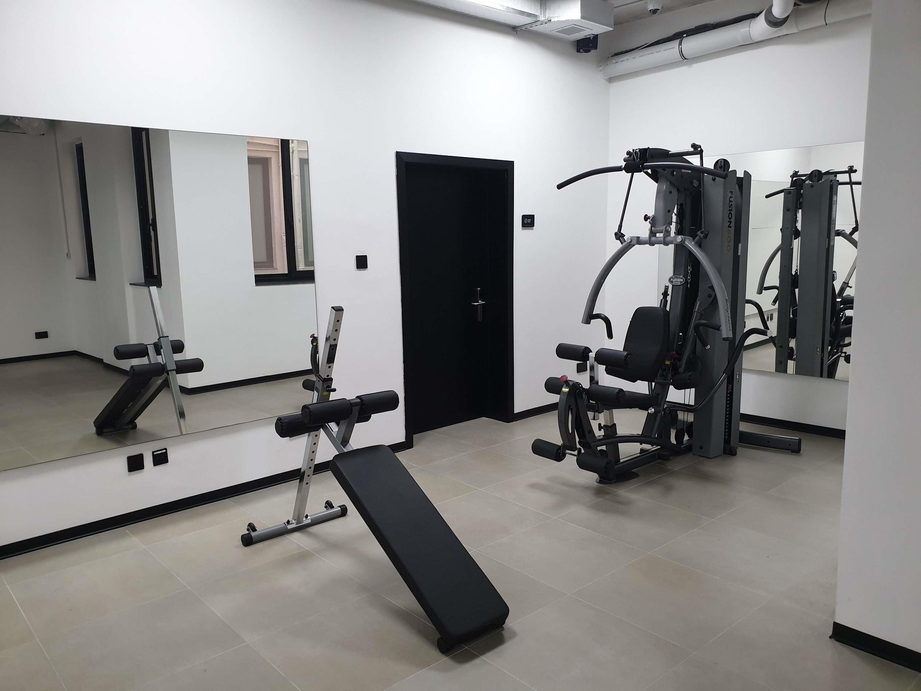 Une salle de sport équipée d’un banc, d’appareils de musculation et d’un miroir.