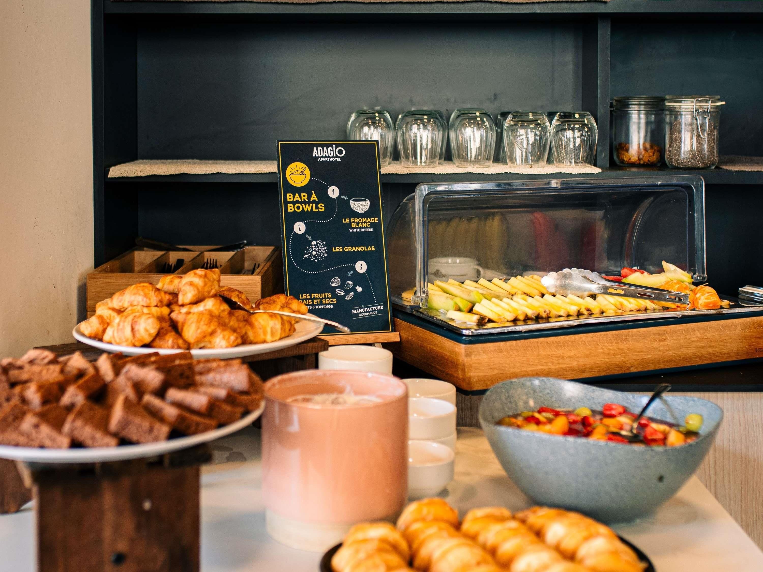 A buffet with croissants, fruits, and a menu board.
