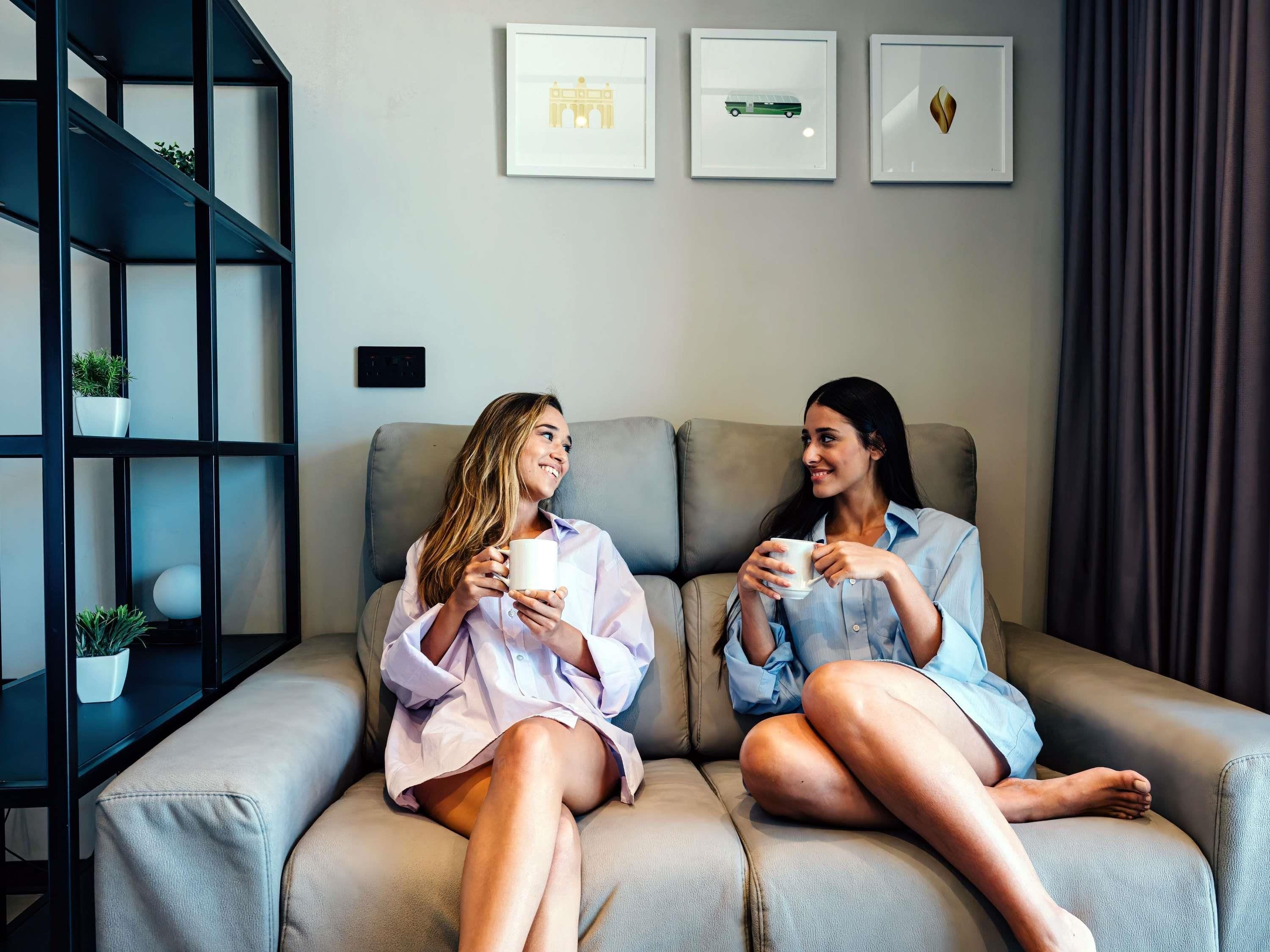 Two people sitting on a sofa in a room with a bookshelf and three framed pictures on the wall.