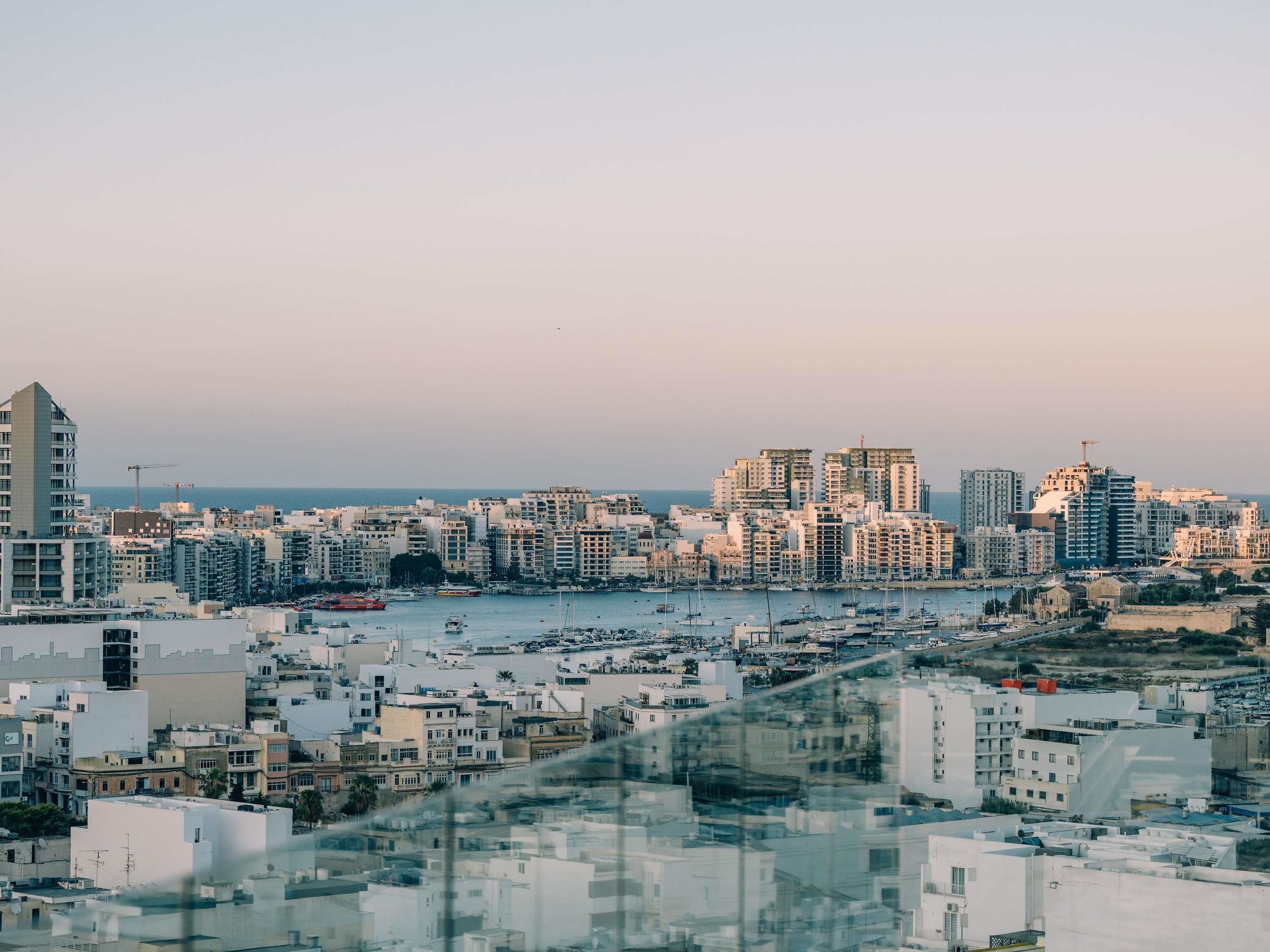 A coastal cityscape with a marina, high-rise buildings, and a clear sky.