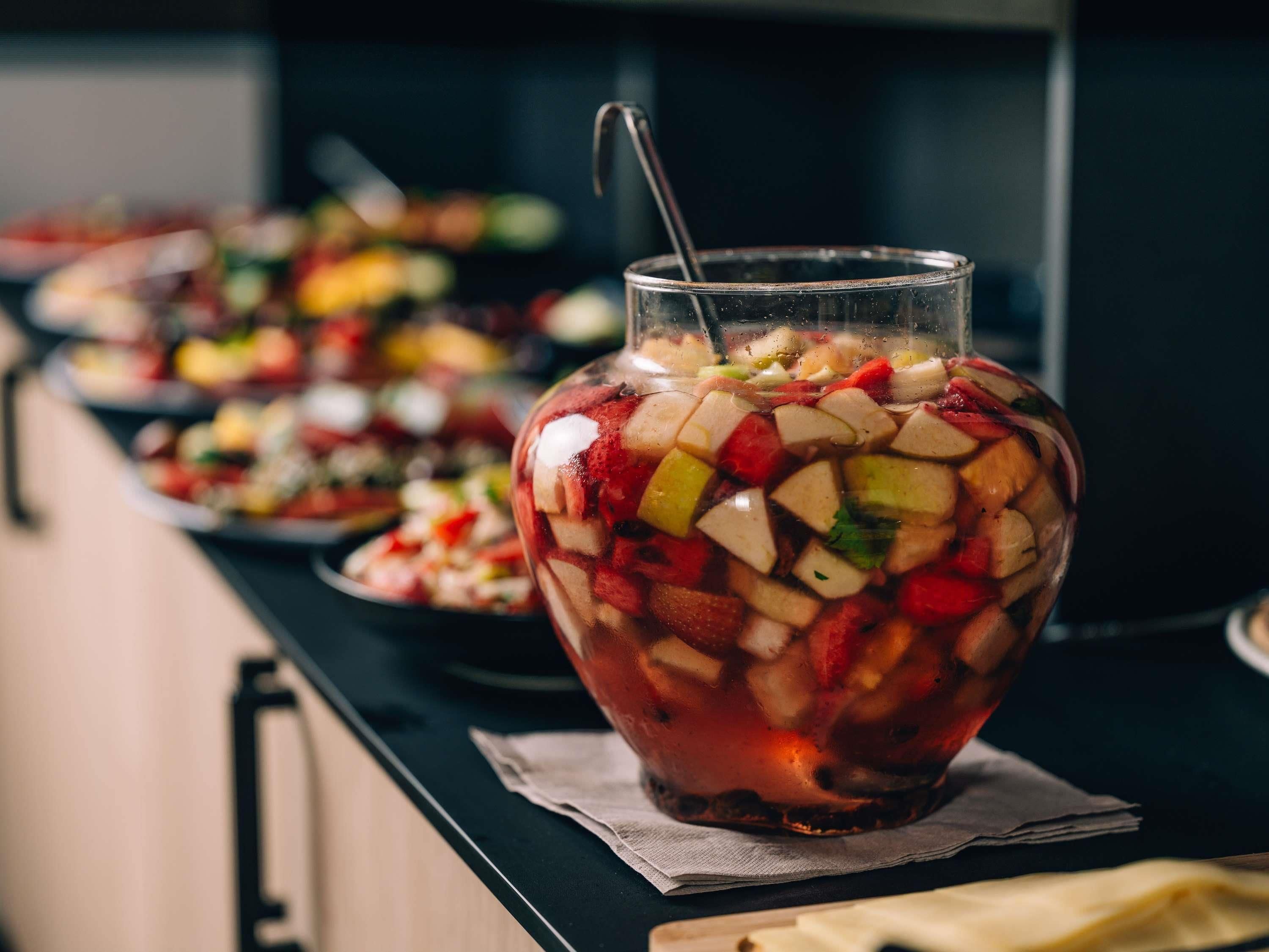 Un jarro de vidrio transparente lleno de ensalada de frutas, sobre una mesa con una servilleta debajo.