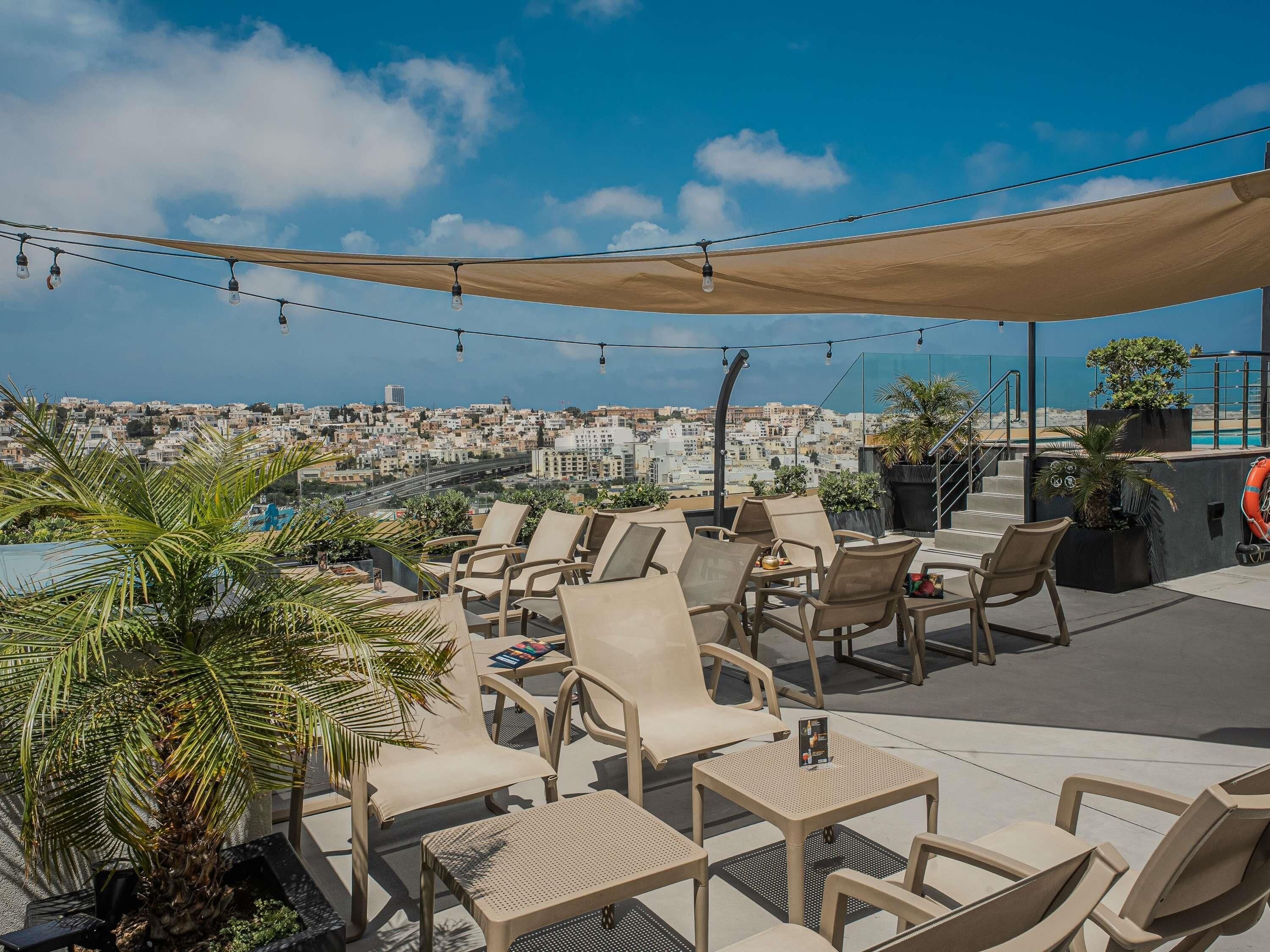Un espacio al aire libre con sillas y mesas, una piscina y vistas a un paisaje urbano.