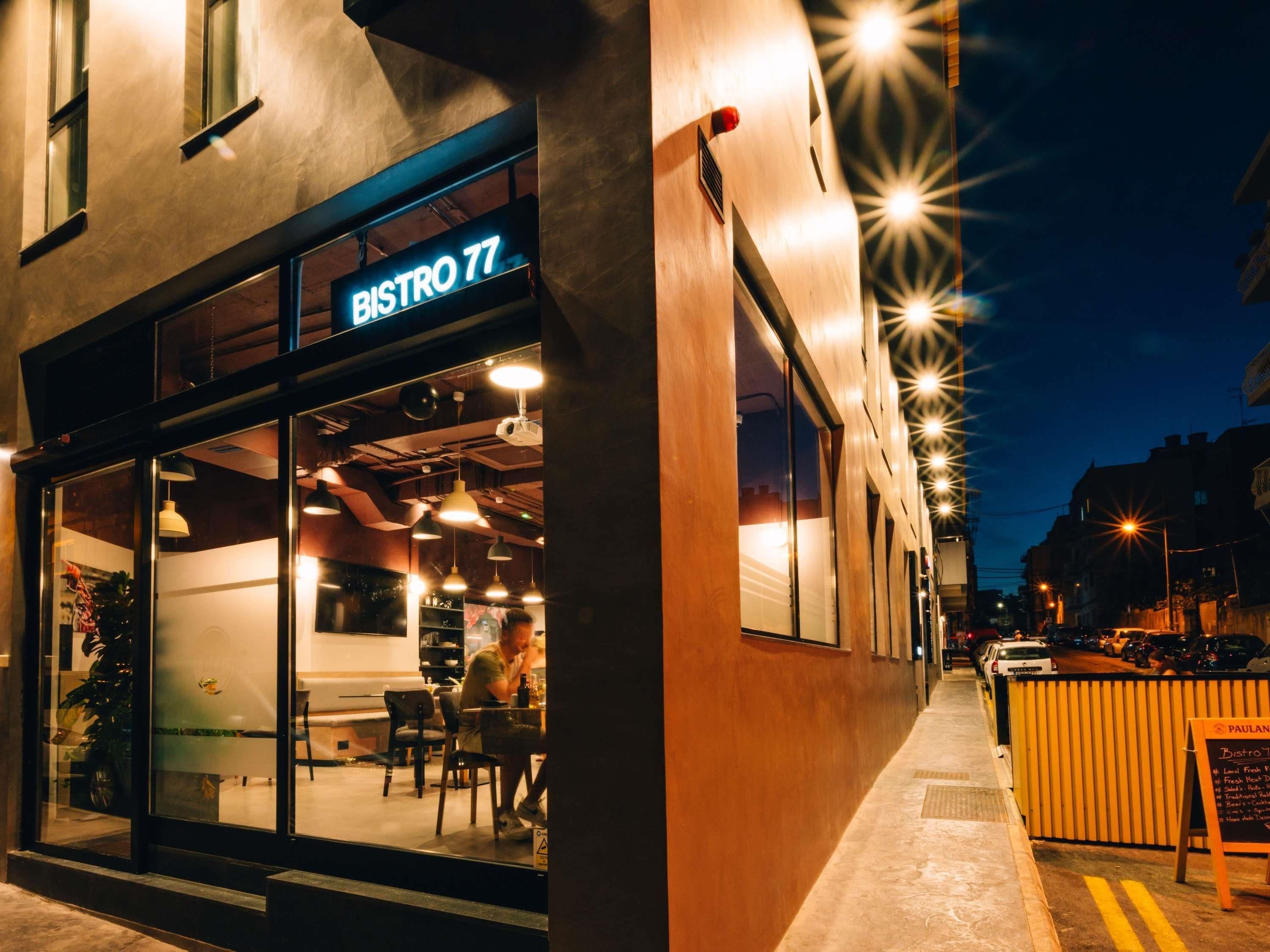 A modern bistro with a glass facade, outdoor seating, and a sign reading "BISTRO 77".