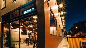 A modern bistro with a glass facade, outdoor seating, and a sign reading "BISTRO 77".