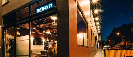 Un bistró moderno con fachada de vidrio, mesas al aire libre y un letrero que dice "BISTRO 77".