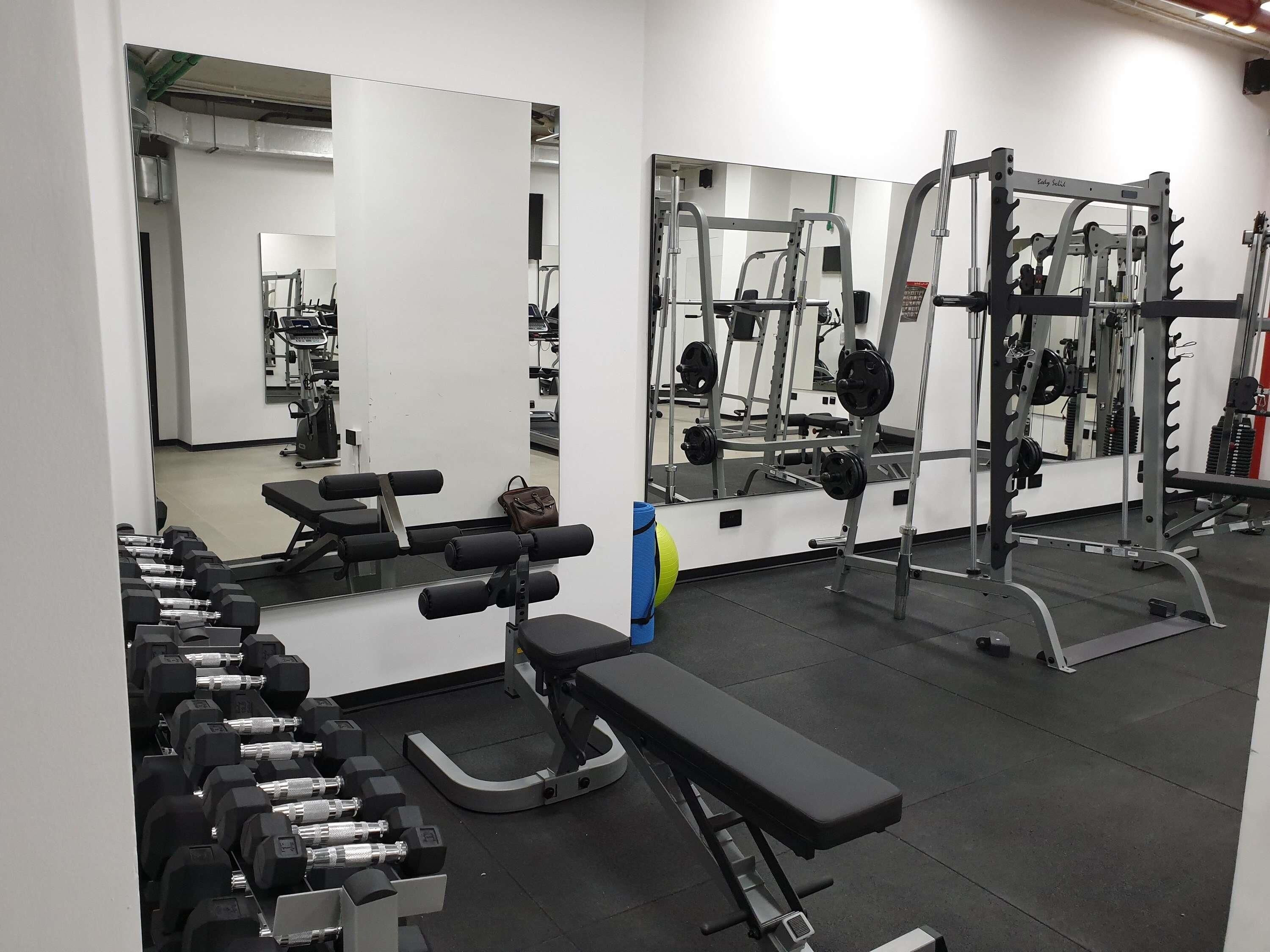 A gym with weightlifting equipment, benches, and mirrors.