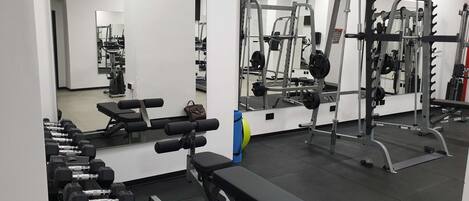 A gym with weightlifting equipment, benches, and mirrors.