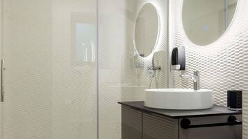 Un baño moderno con ducha de vidrio, espejo redondo y lavamanos blanco.