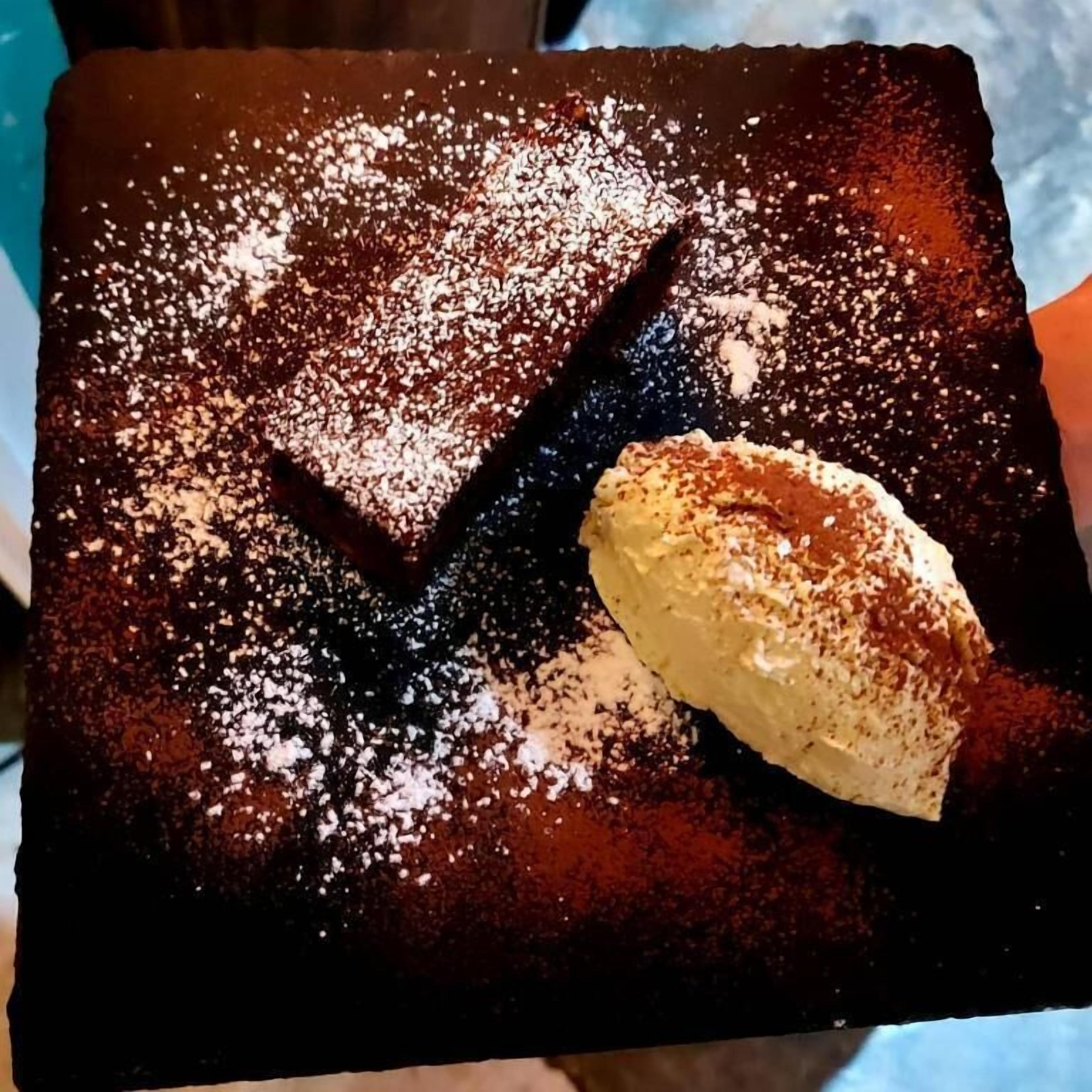 A dessert with powdered sugar and a scoop of ice cream on a dark plate.