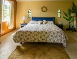 A bedroom with a bed, two nightstands, a lamp, a plant, and a window with a wreath.