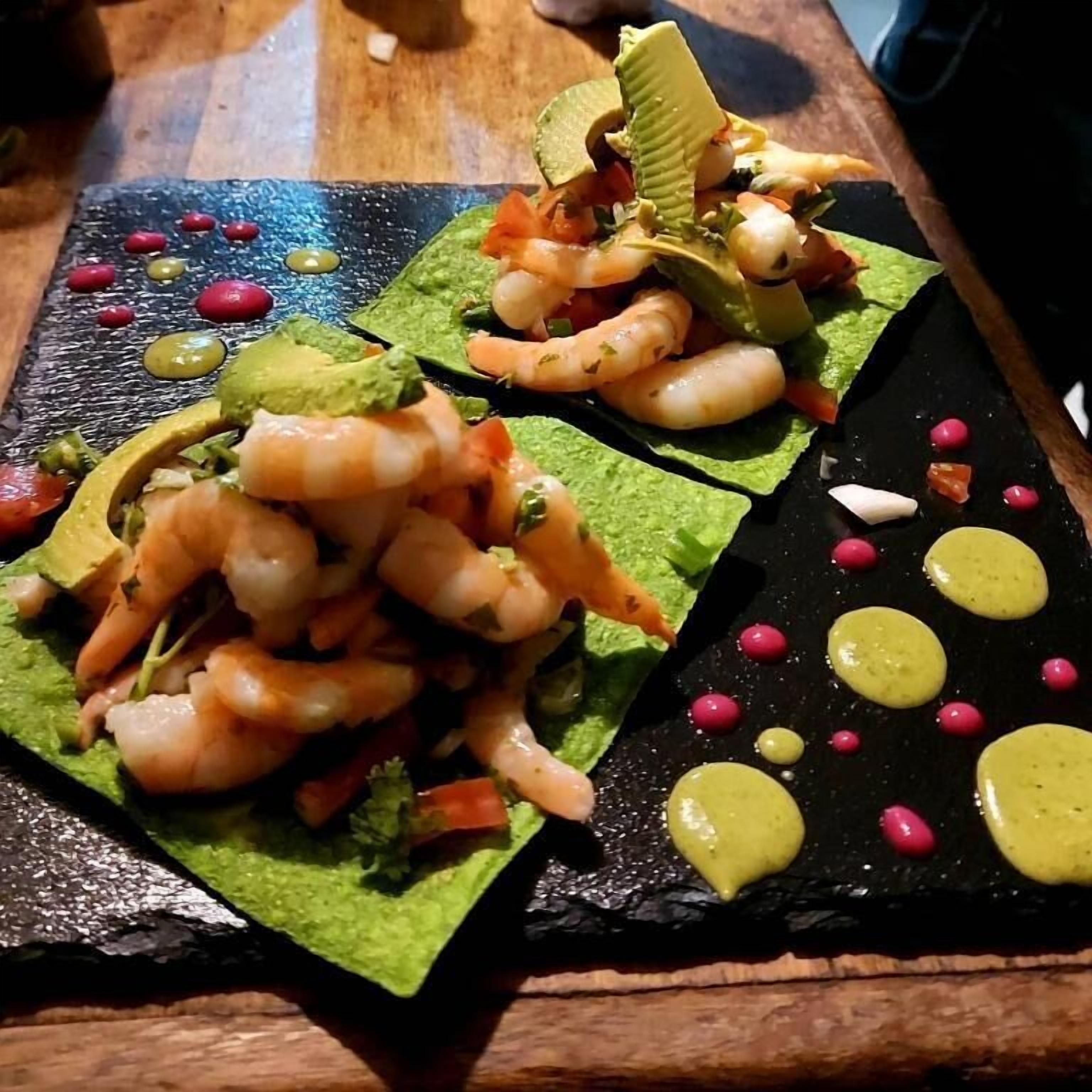 Ein Fischgericht mit Garnelen und Avocado auf einer schwarzen Schieferplatte.