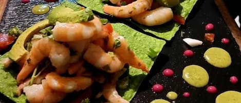 Plato de mariscos con camarones y aguacate sobre una losa de pizarra negra.
